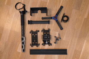 Here are all the ingredients for this 'magic soup': a cage built from two cheese plates, four carbon rods, and four rod clamps. One of the cheese plates features an Arca-Swiss clamp mounted upside down, while a foldable center column is attached to the lower cheese plate. A monopod foot acts as the base, with the monopod itself mounted in an inverse position. Finally, at the top (well, technically the bottom), there is a mobile phone clamp and a 3D-printed hood. The design was inspired by various low-angle solutions I discovered online.